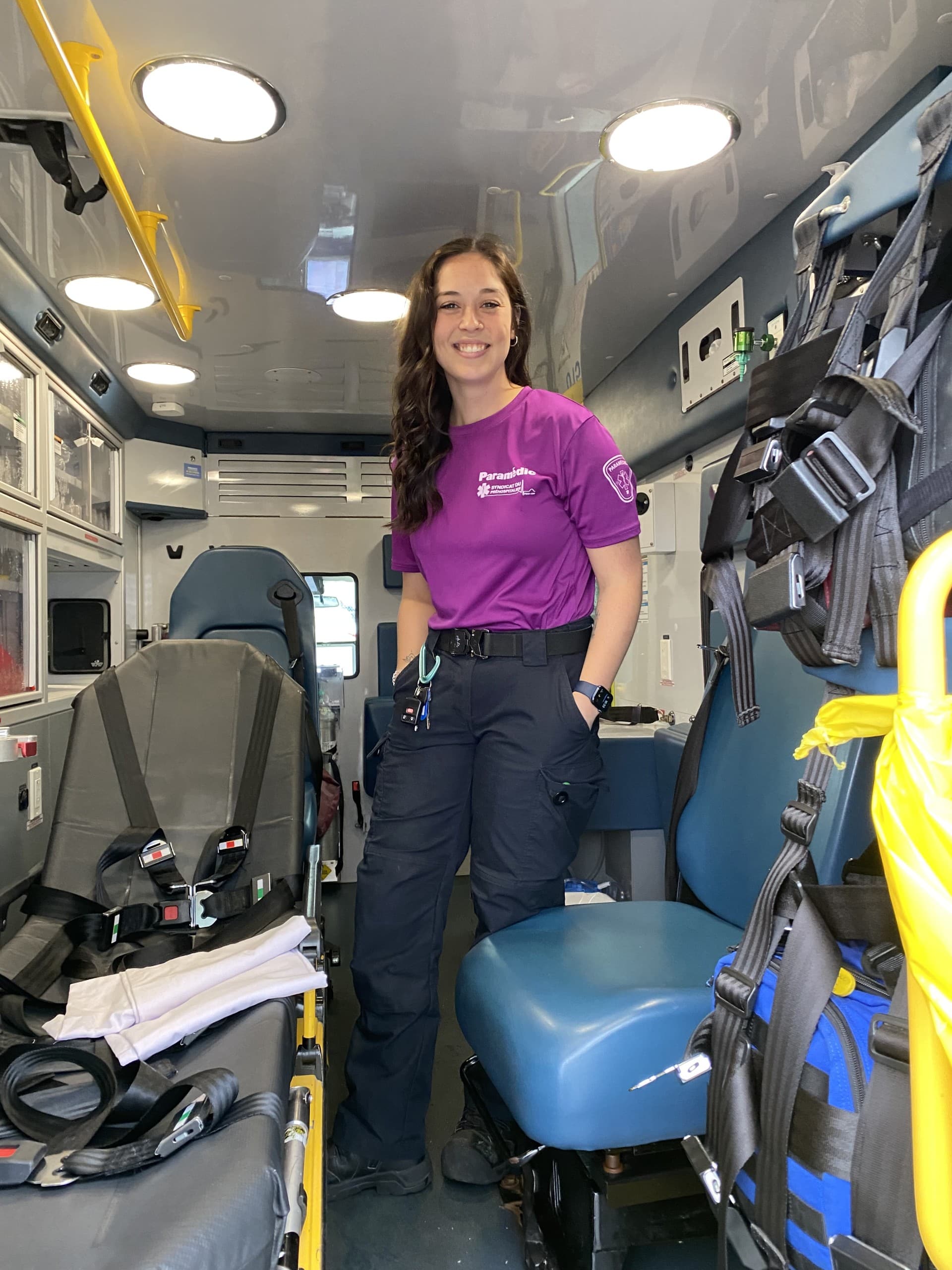 Alyson Caron, a paramedic, stands in an ambulance. She is looking at the camera and smiling.